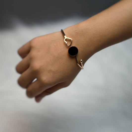 Stylish open bangle bracelet in rose gold with modern shapes and a central black enamel disc.