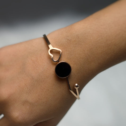 Close-up of a minimalist rose gold bracelet featuring a heart motif and glossy black charm.