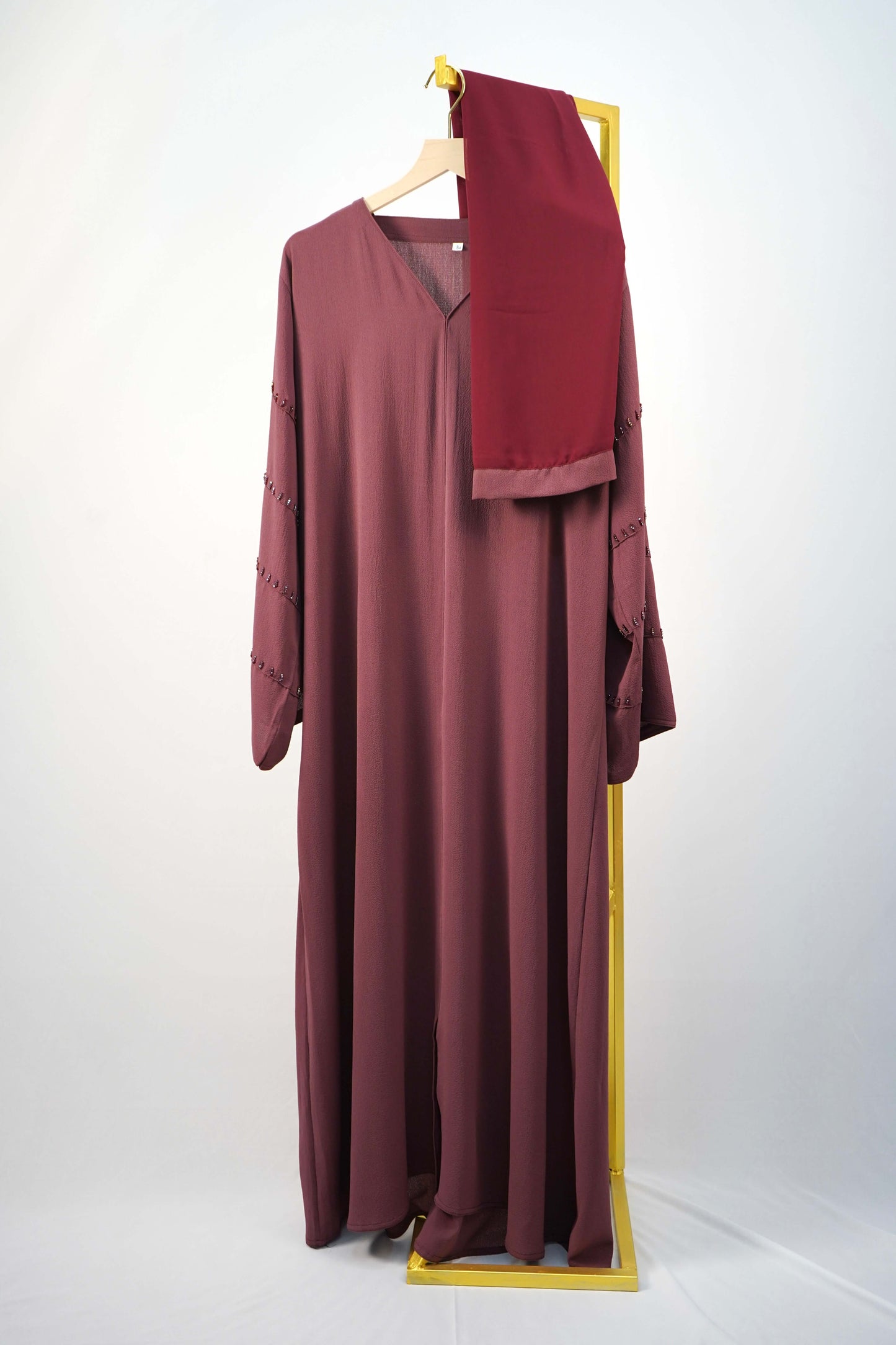 A full shot of the Korean Bubble Abaya in Old Mauve, hanging with its matching scarf, emphasizing the luxury fabric and design.