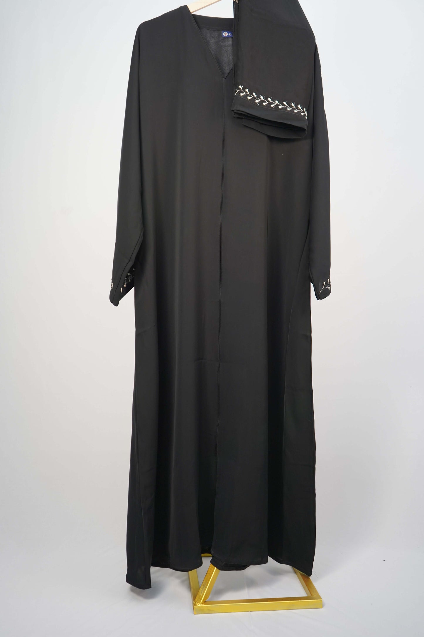 The black Korean Nidha Abaya with white leaf-like embroidery, hanging with a matching scarf.