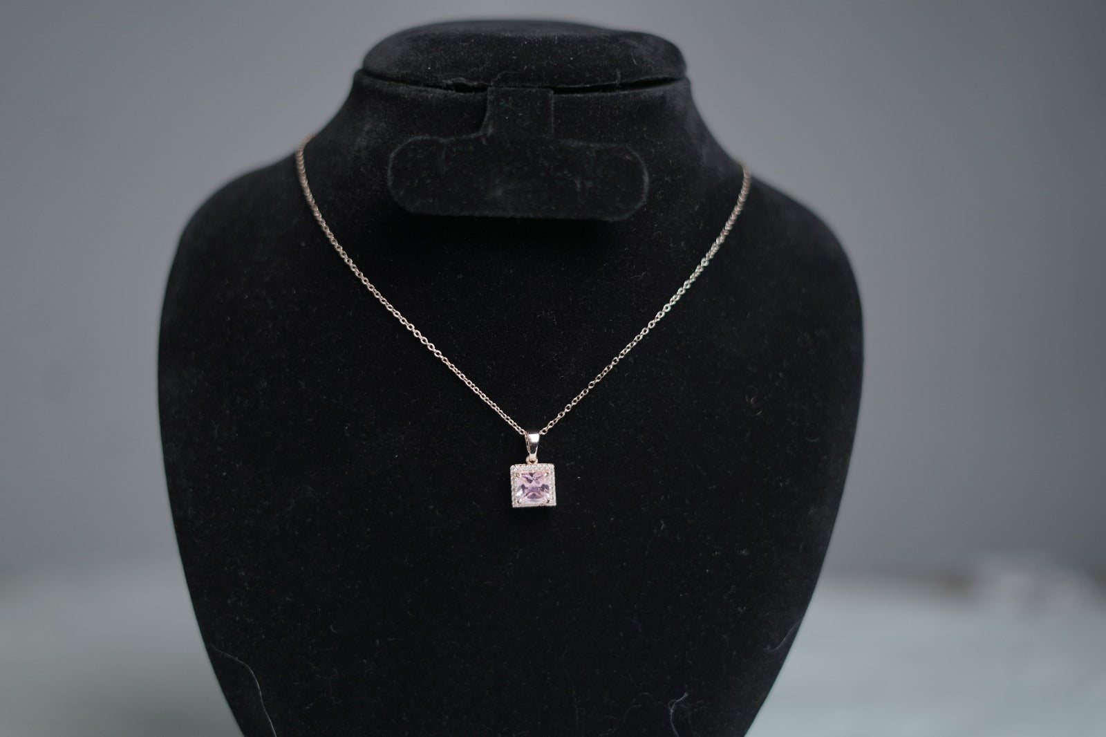 Lavender cubic zirconia necklace with gold chain on jewelry stand.