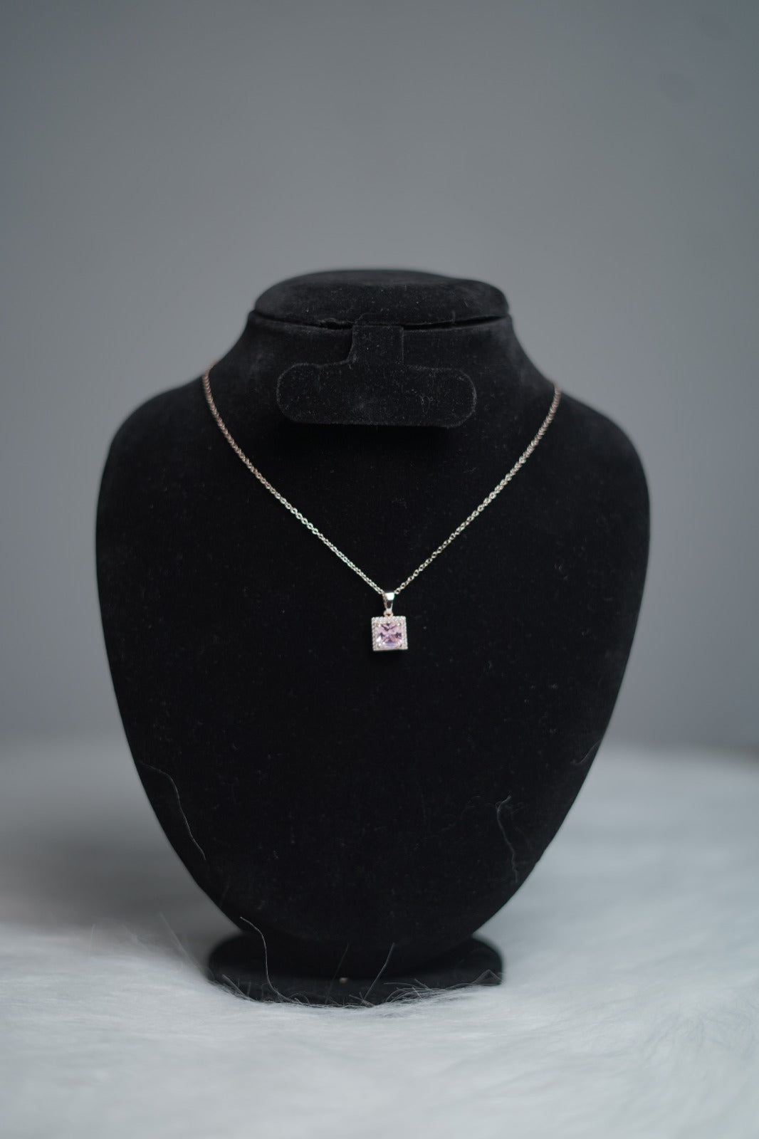 Princess-cut lavender pendant styled on necklace holder for showcase.