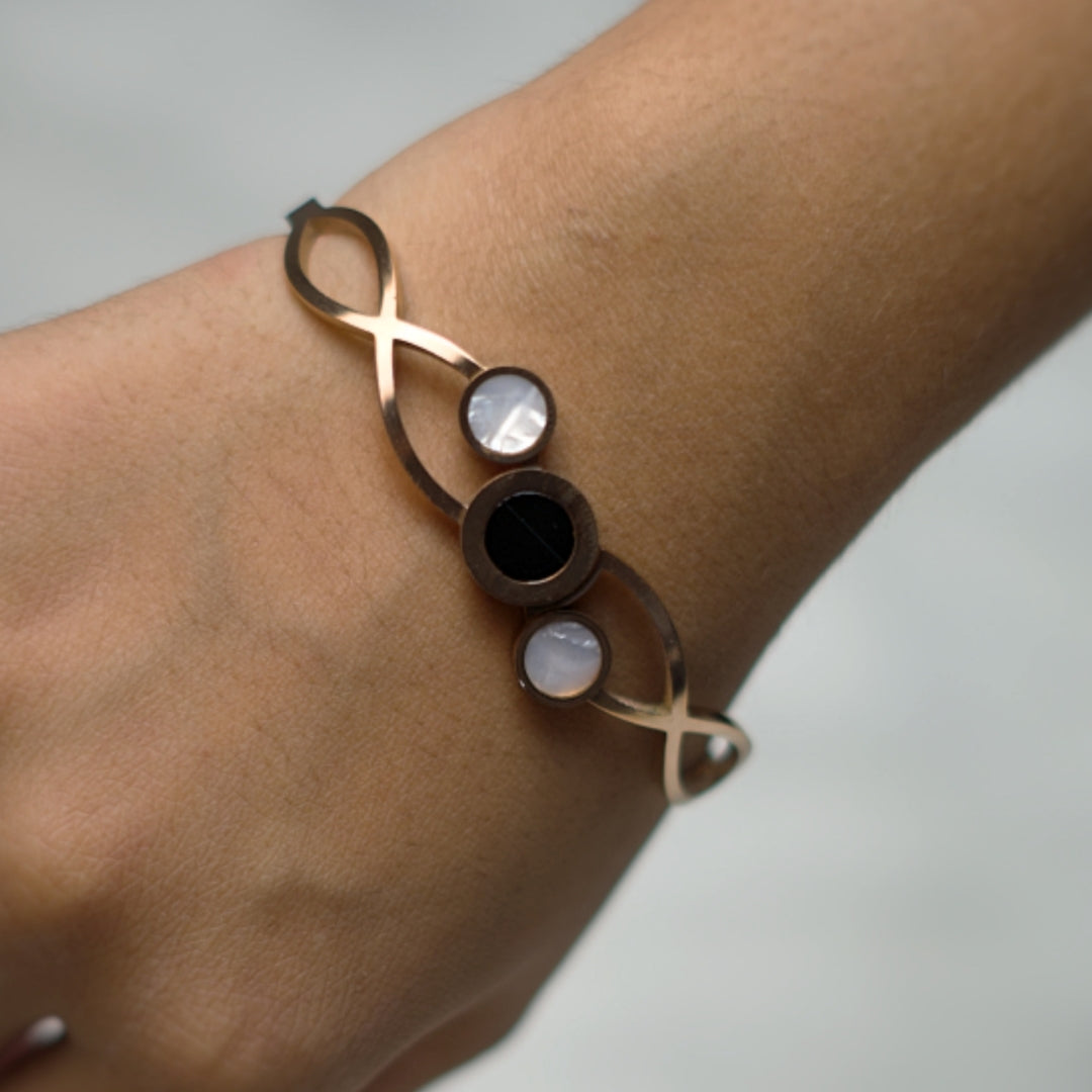 Geometric rose gold bangle bracelet with contrasting round stones and an infinity-inspired design.