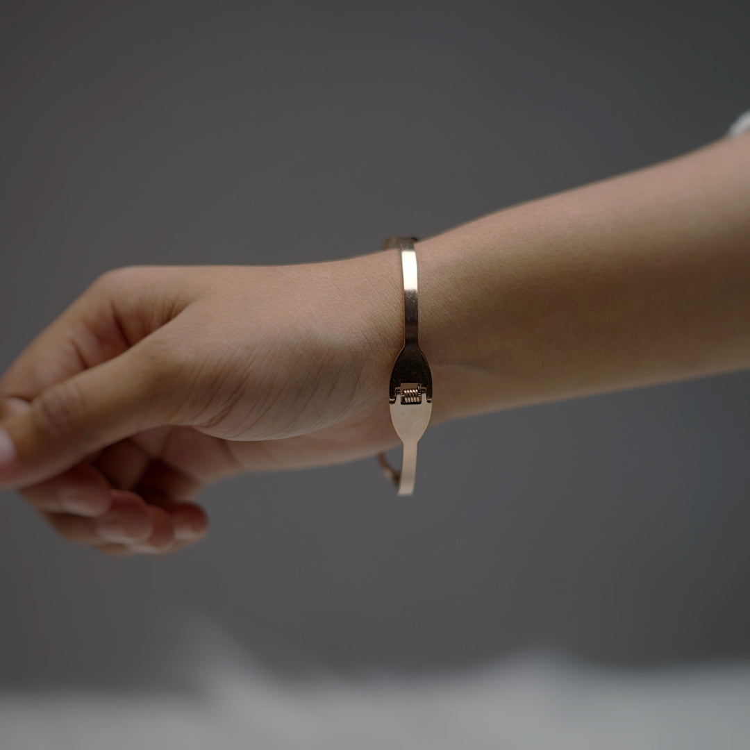 Back view of the rose gold bangle on a wrist, showing the push-lock clasp mechanism.