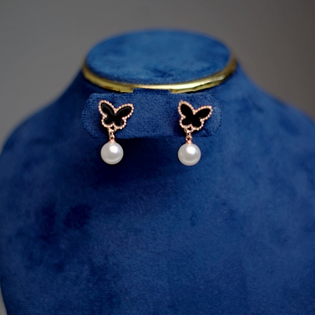 Close-up of delicate rose gold and black butterfly pearl drop earrings, perfect for stylish everyday wear.