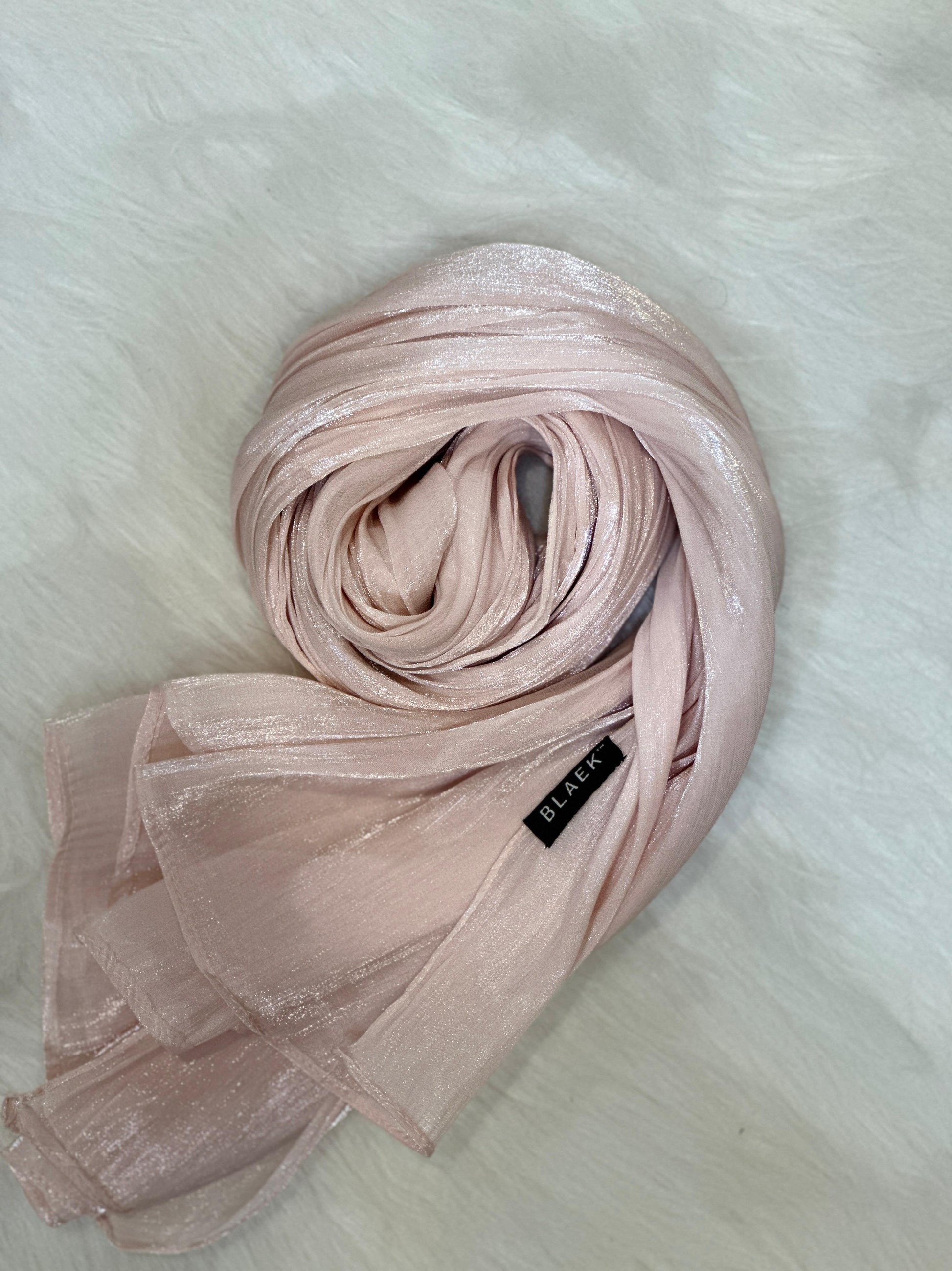 Pastel pink shimmer hijab folded in a rounded form, emphasizing its graceful finish.