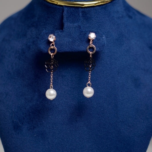 Close-up of rose gold dangle earrings with intricate floral design and classic white pearls.