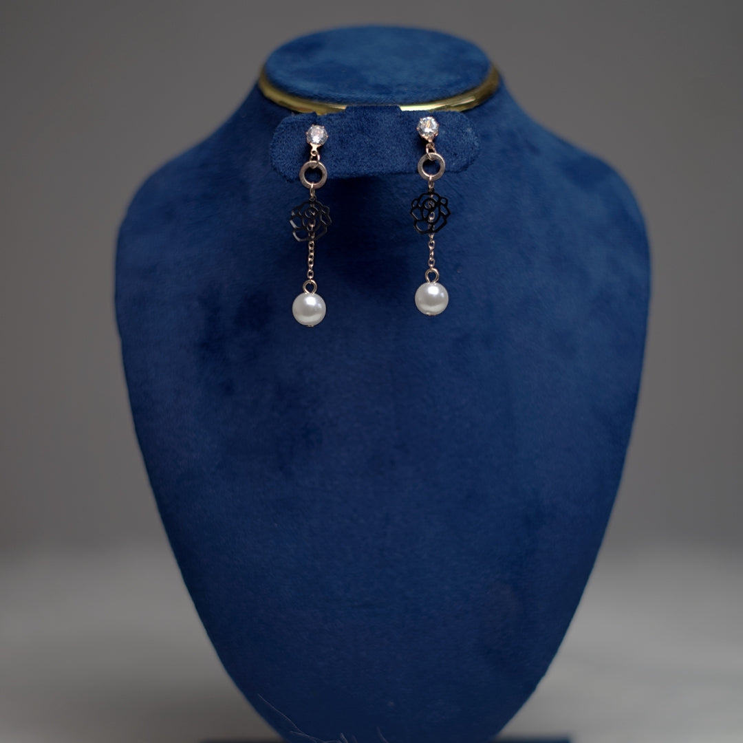 Elegant pearl drop earrings featuring a black flower charm and clear crystal stud, displayed on a dark blue velvet stand.