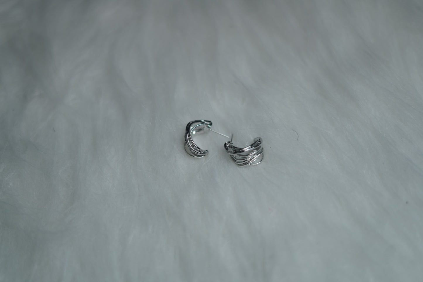 Mini silver hoop earrings with fold detailing placed on soft fur base.