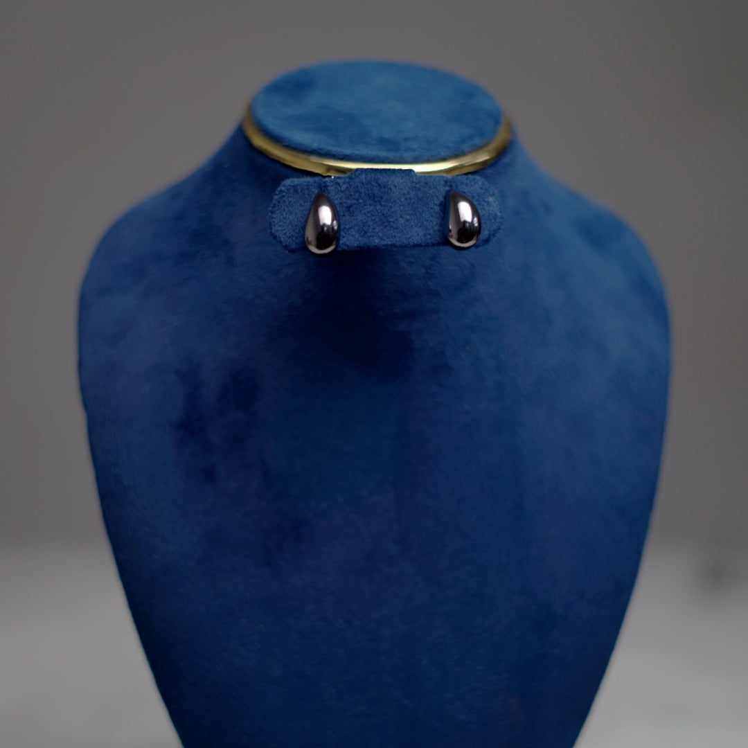 A pair of polished silver teardrop stud earrings displayed on a deep blue velvet stand.