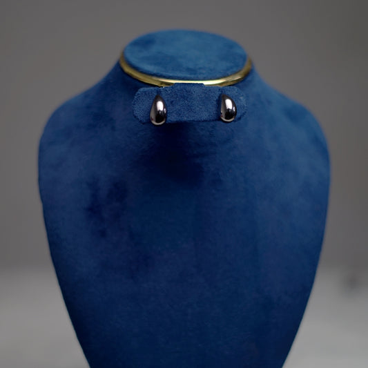 A pair of polished silver teardrop stud earrings displayed on a deep blue velvet stand.