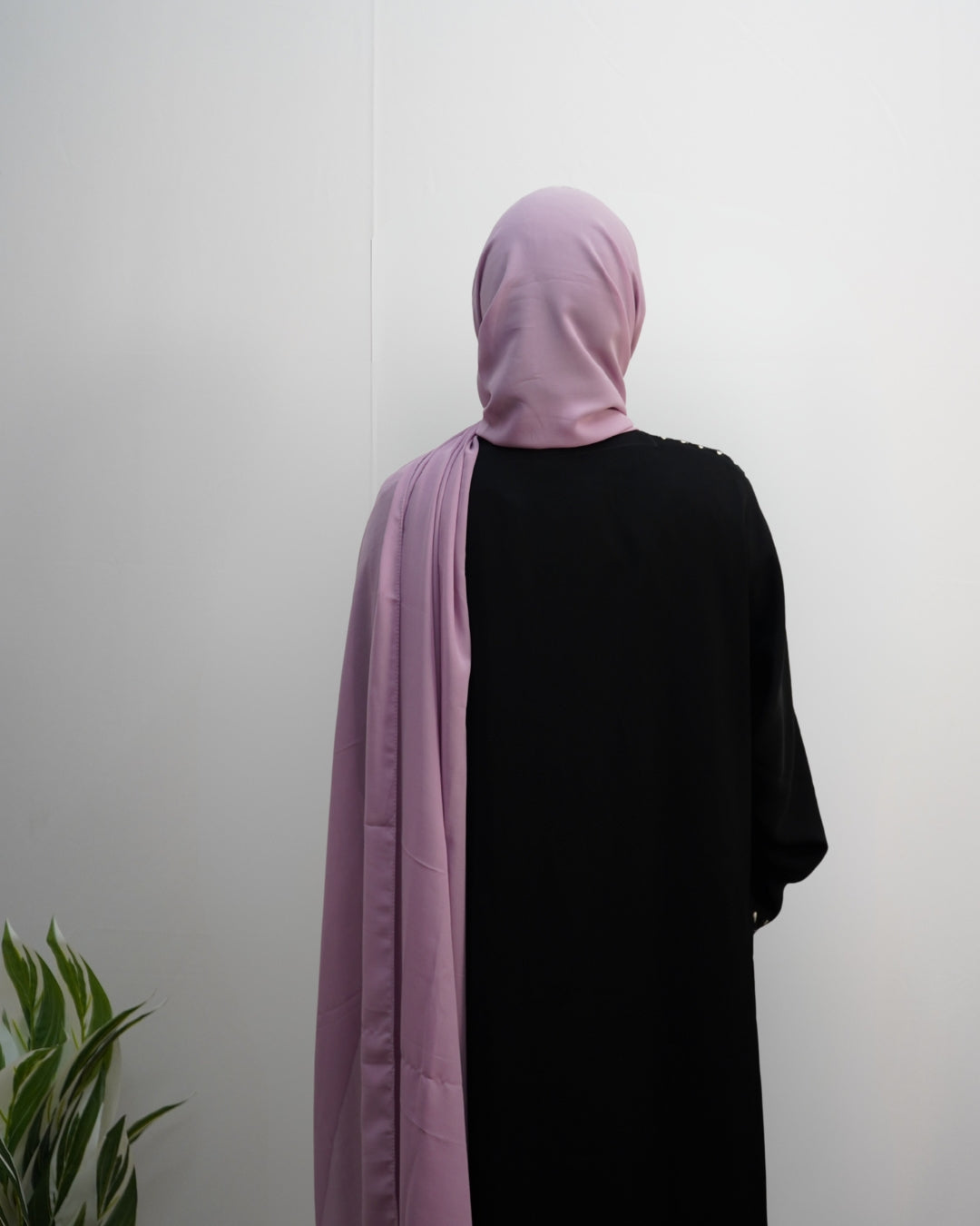 Woman wearing a soft lilac indian chiffon hijab styled over a black abaya, back view.