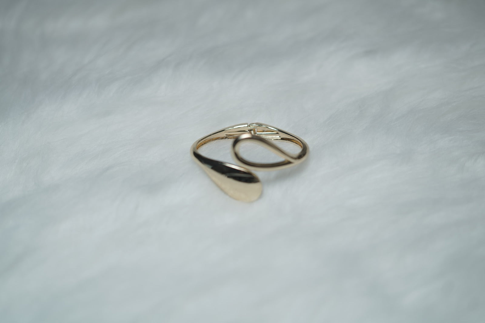 Open-ended gold bangle with sculptural teardrop design photographed on plain background.