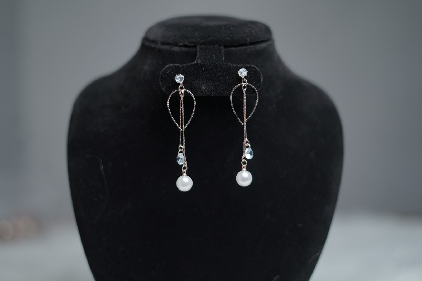 Elegant wedding-style pearl earrings on jewelry display stand.