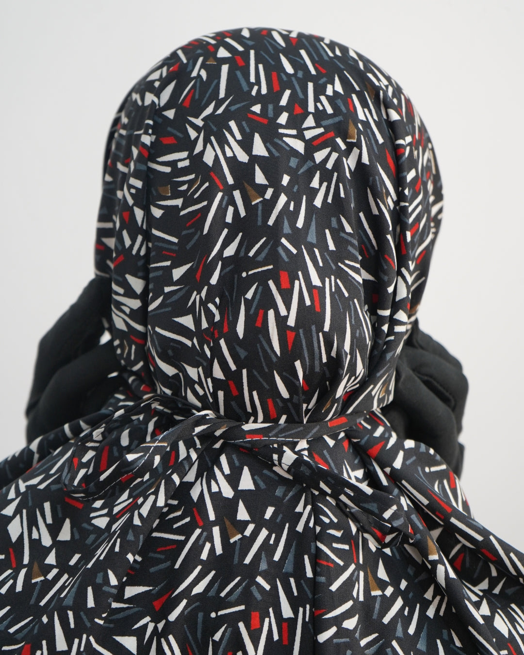 Close-up of black prayer dress back tie with abstract red, white, and grey print.