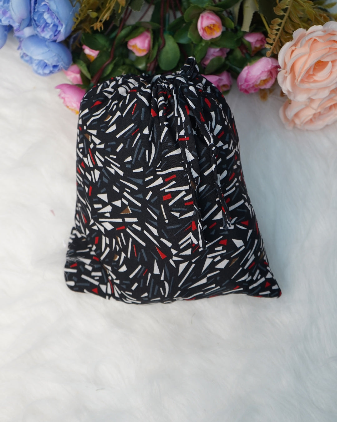 Compact matching fabric pouch in black abstract print placed on white fur background.