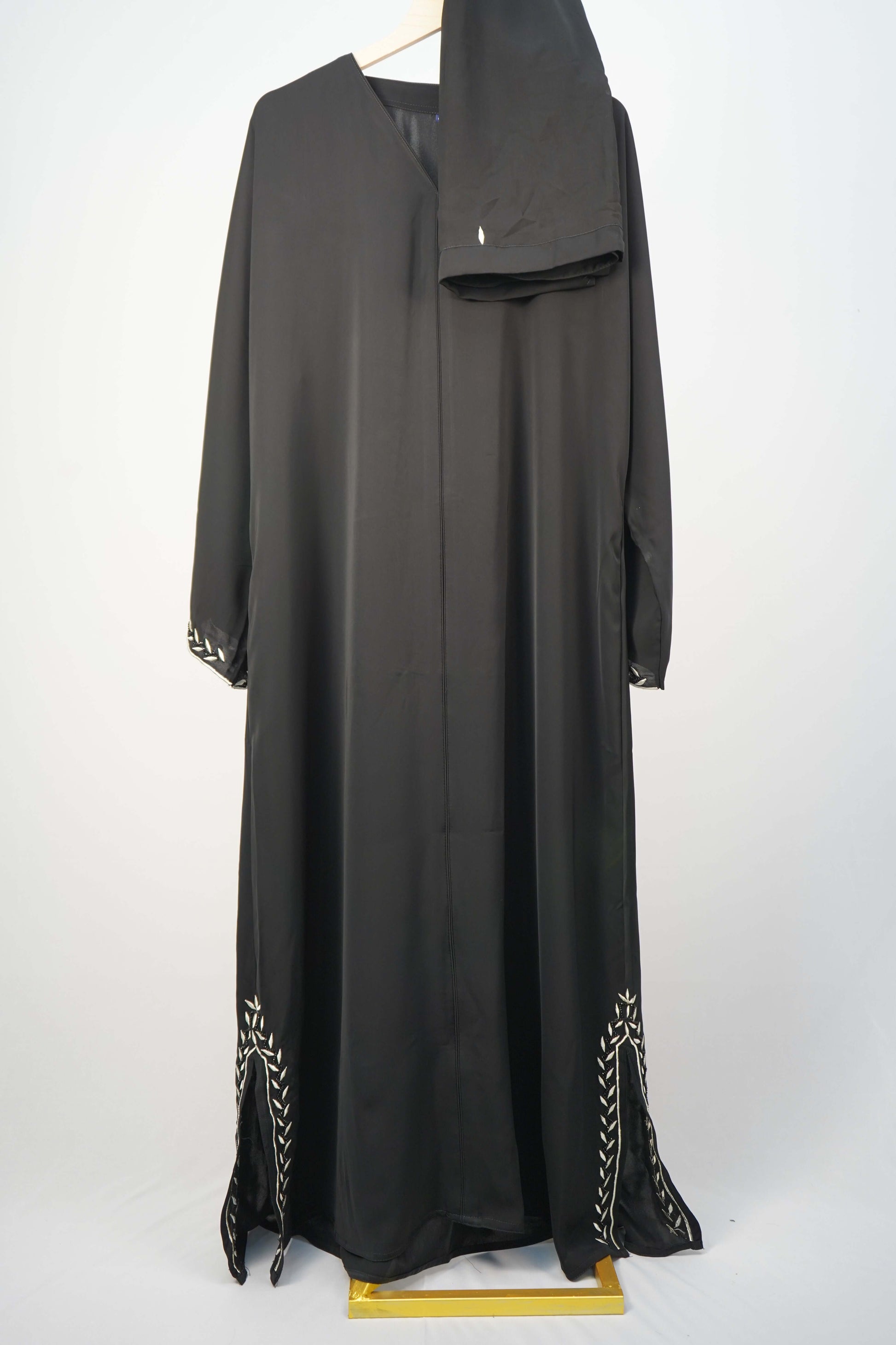The classic Korean Nidha Abaya in black, hanging with a matching scarf to showcase its full design and contrasting white leaf embroidery.
