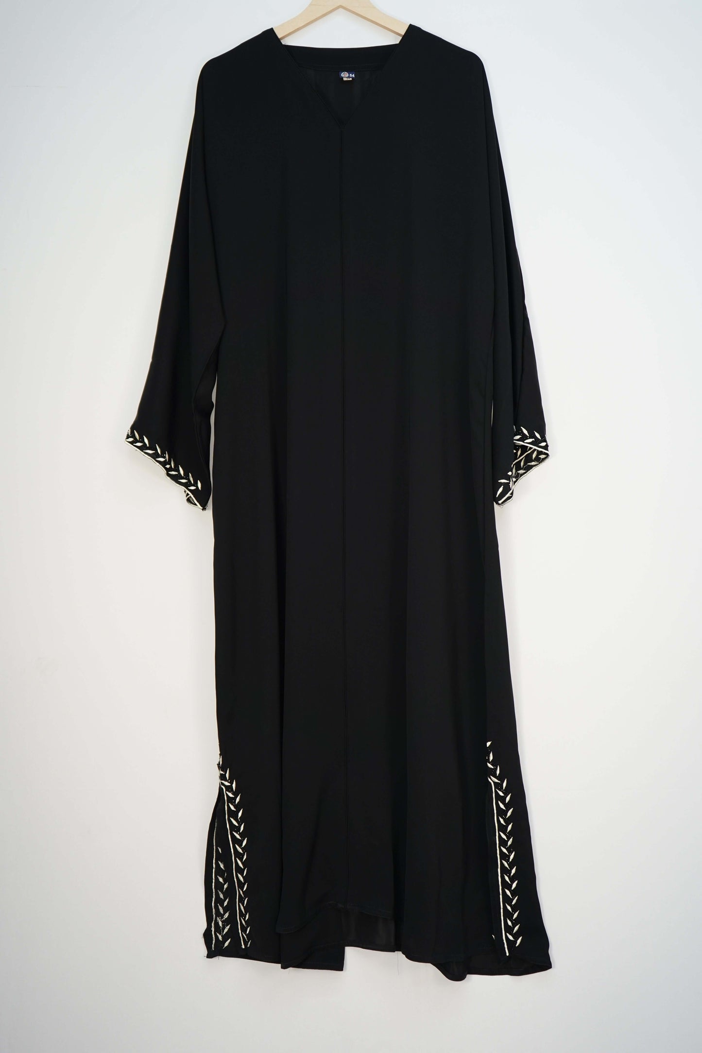 A full shot of the black Korean Nidha Abaya hanging, highlighting the silky fabric, V-neck, and white embroidery on the hem and sleeves.