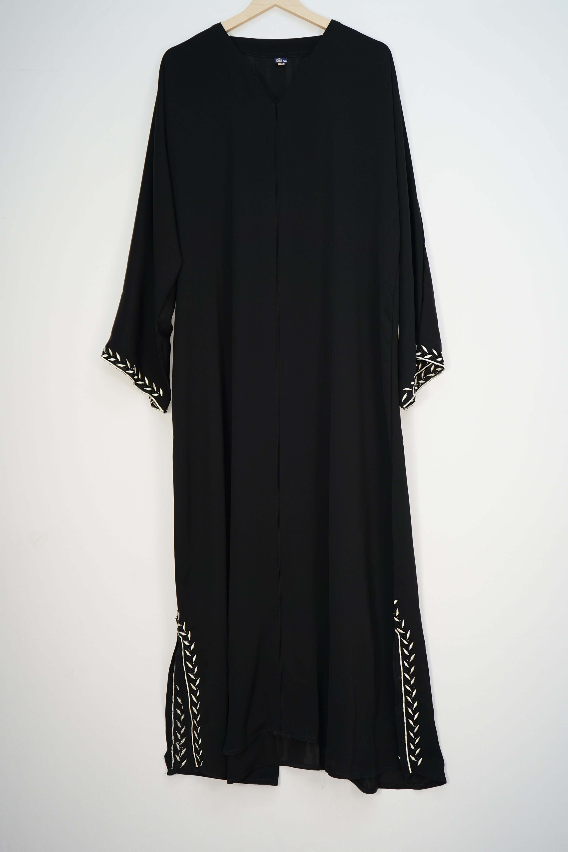 A full shot of the black Korean Nidha Abaya hanging, highlighting the silky fabric, V-neck, and white embroidery on the hem and sleeves.