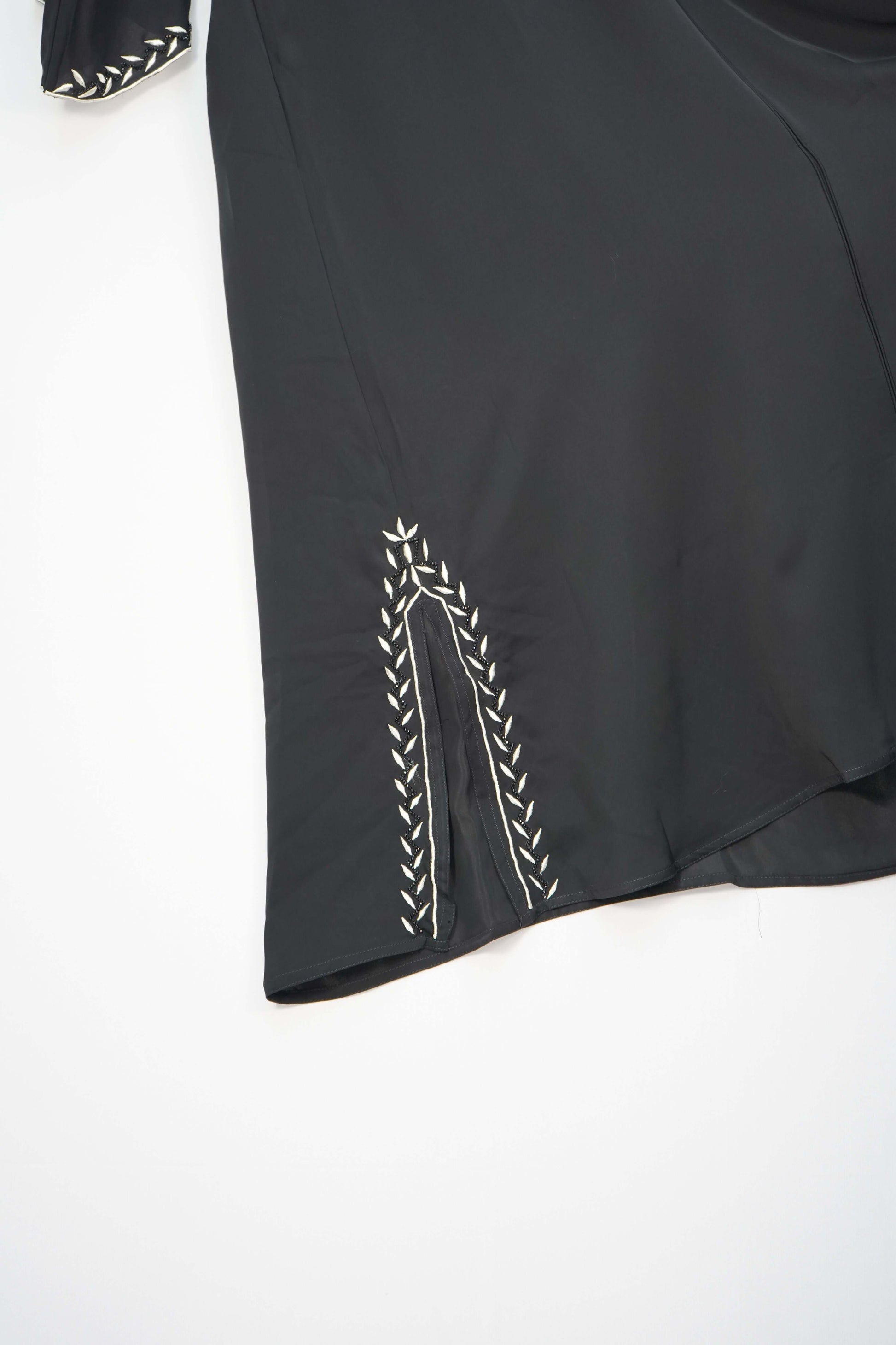 A close-up of the detailed white leaf-like embroidery on the side slit of the black abaya's hem.