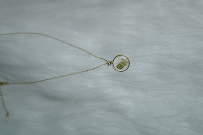 Gold chain necklace with resin floral pendant on minimal white surface.