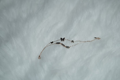 Flatlay of butterfly bracelet resting on fluffy white fur, highlighting soft-toned elegance.