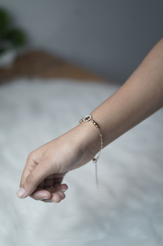 Dainty rose gold bracelet styled on hand, with a celestial-themed charm at the center.