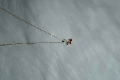 Red and green crystal cherry necklace laid on white background.