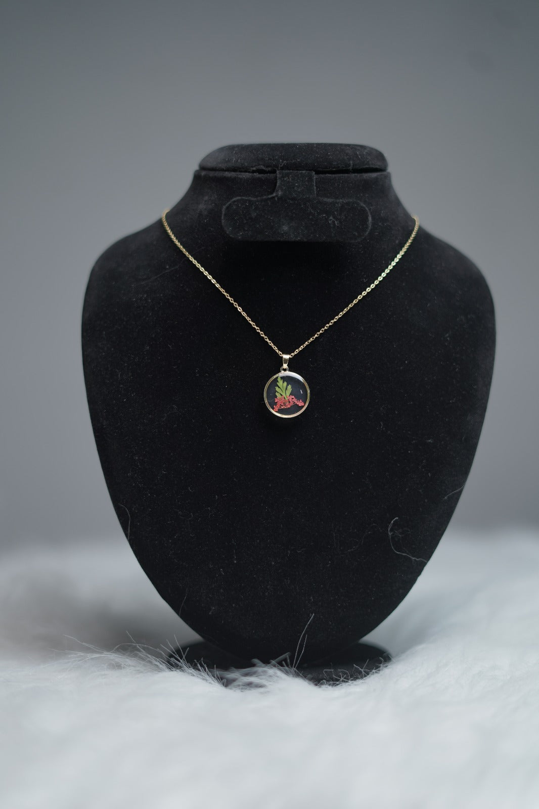 Round resin pendant necklace with red floral design displayed on stand.