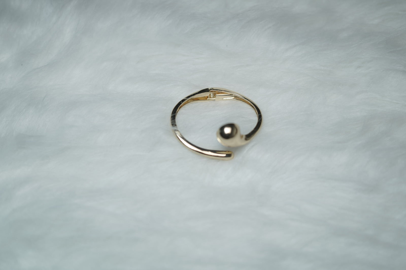 Modern gold cuff bracelet with molten swirl ends on plain surface.