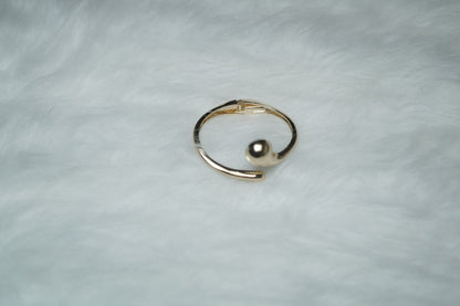 Modern gold cuff bracelet with molten swirl ends on plain surface.