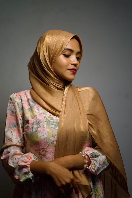 Chiffon hijab in warm gold shimmer, draped in a smooth, polished finish.