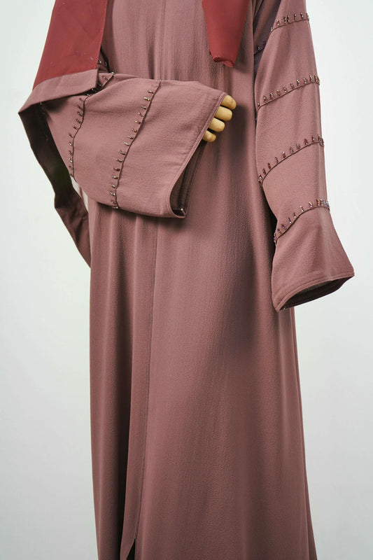 A front view of a woman wearing the Korean Bubble Abaya in Old Mauve, showcasing the elegant drape and the studded sleeves.