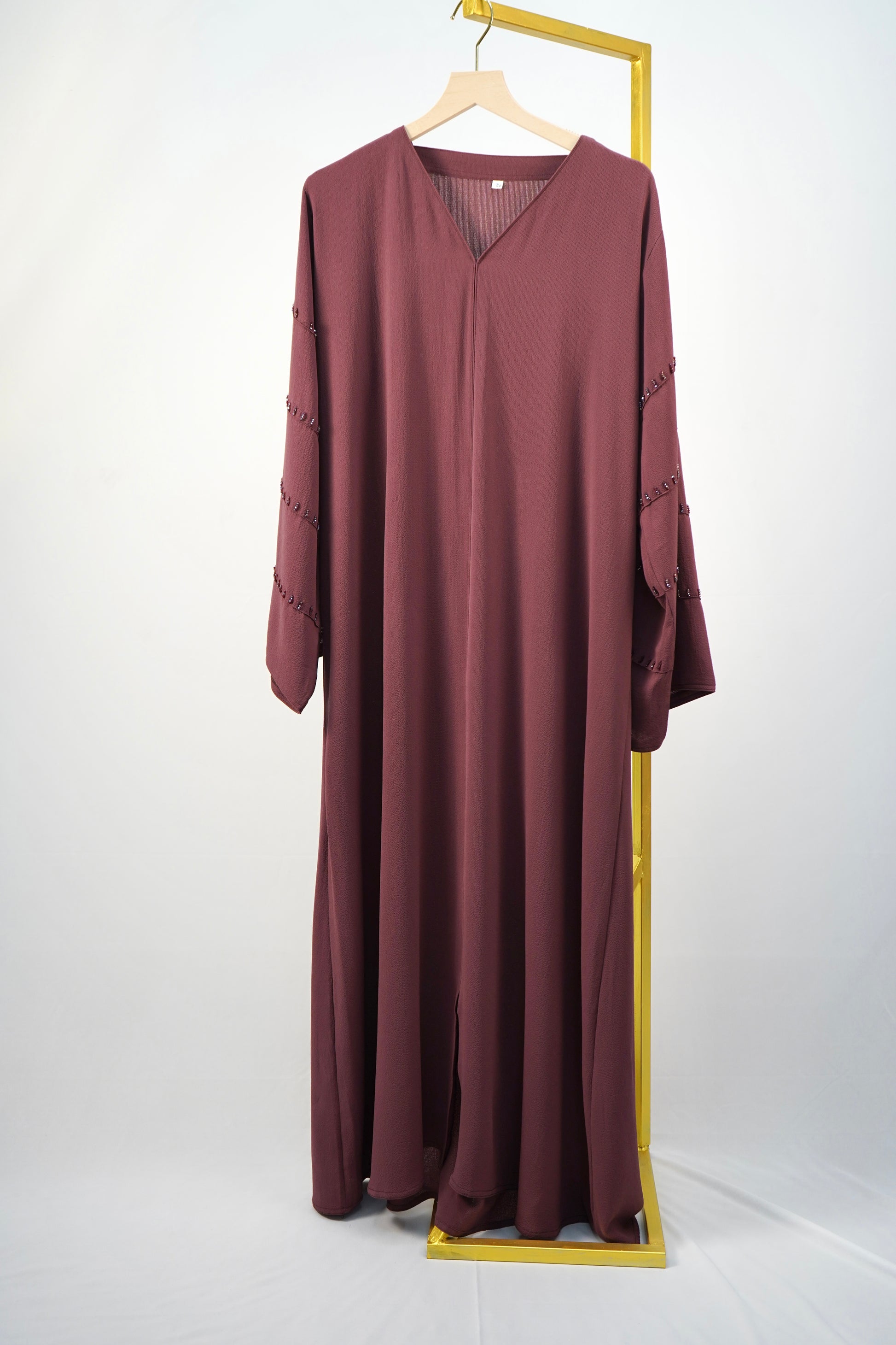 A full shot of the Korean Bubble Abaya in Old Mauve, hanging to highlight its silky texture, V-neck, and the unique studded sleeves.