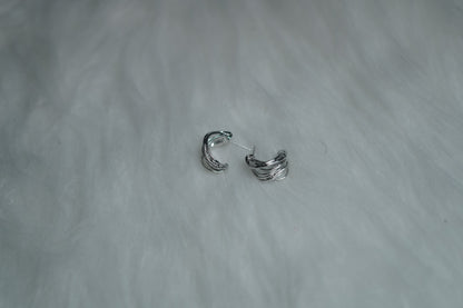 Mini silver hoop earrings with fold detailing placed on soft fur base.