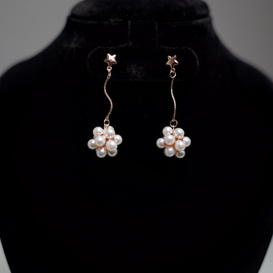 Close-up of star-top earrings with curved metallic lines and pearl flower detailing at the base, giving a soft and charming look.