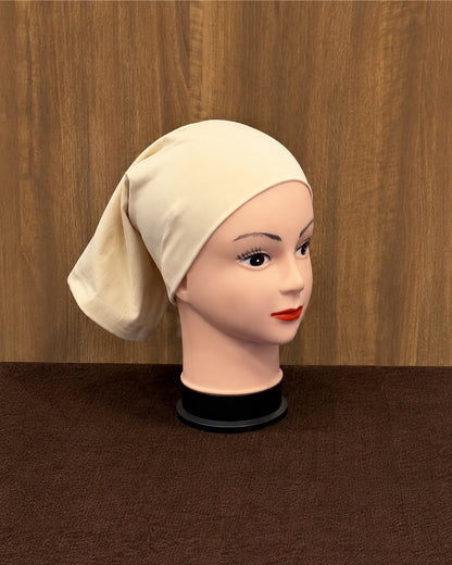 A vanilla-colored inner cap wrapped around a mannequin head, displayed on a black stand against a brown wood-paneled background.