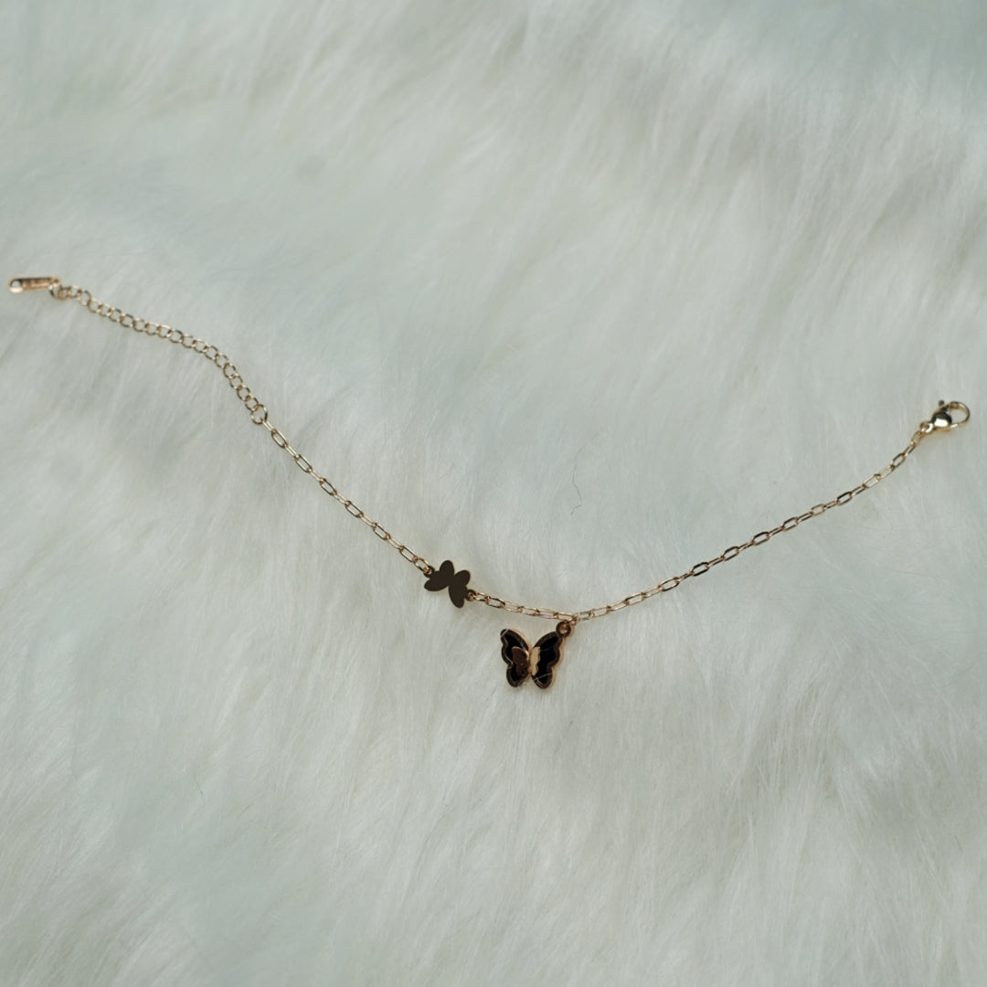 Twin butterfly charm bracelet resting on fuzzy textured background.