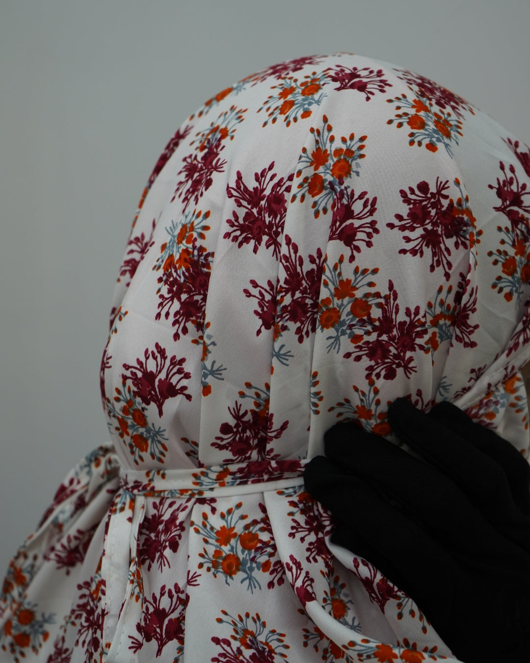 Detailed view of gathered head covering with tie on floral prayer dress.