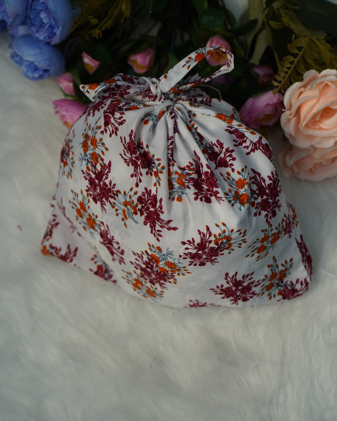 Matching pouch in white floral fabric, placed on soft surface with flowers.