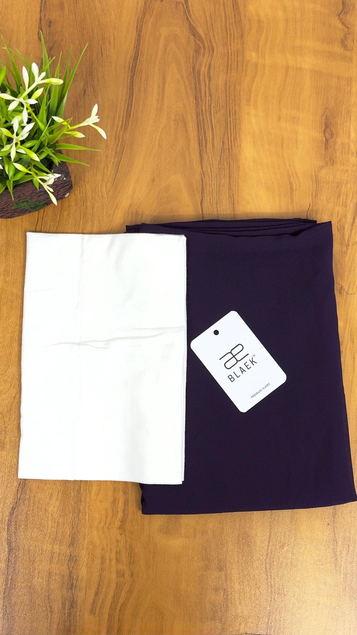 Neatly folded white cap with eggplant hijab on a plain background.