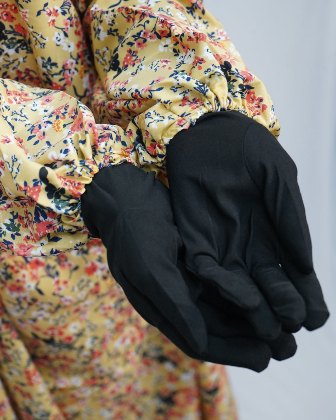 Elasticated sleeve of yellow floral prayer dress paired with black gloves for modest coverage.